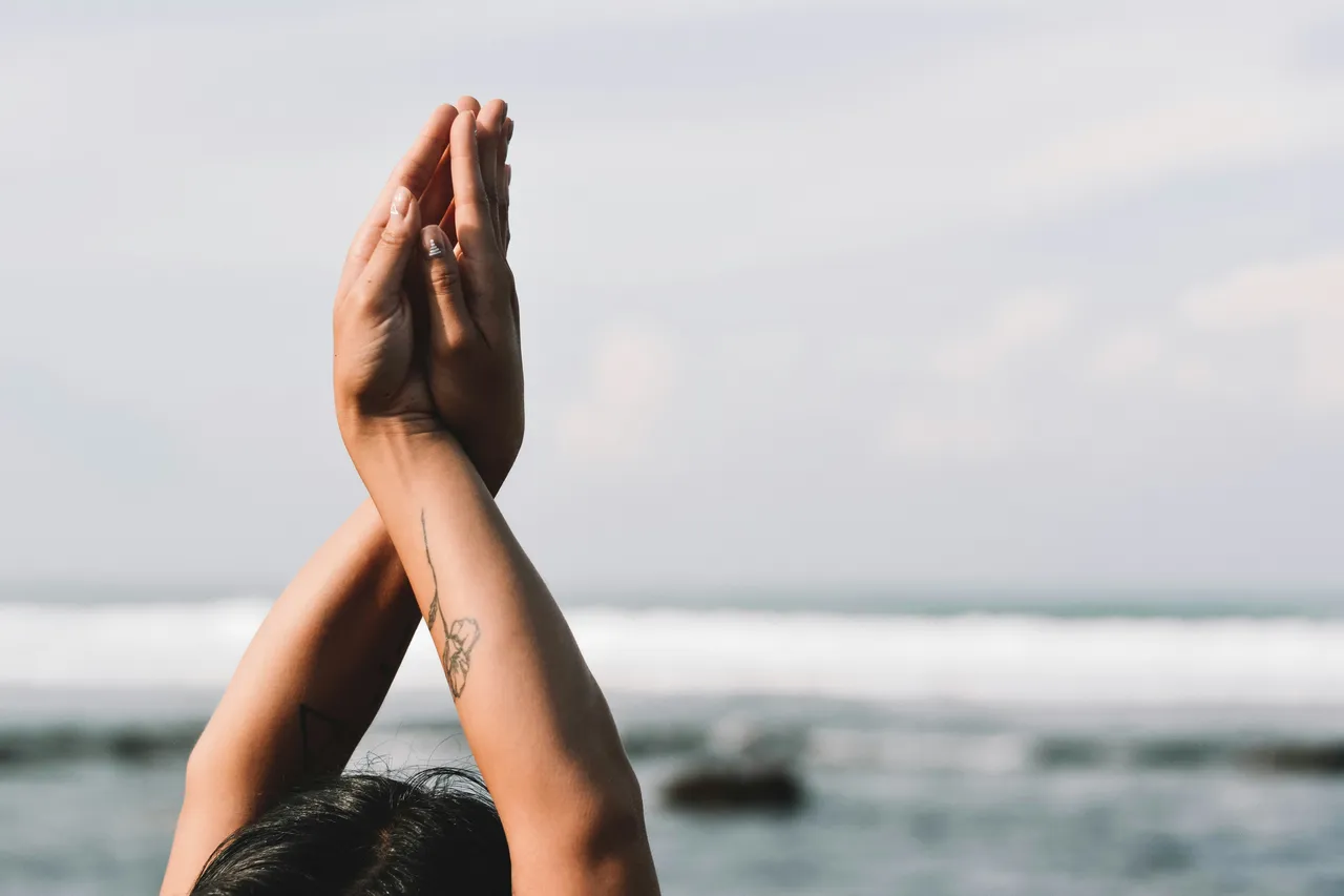 Hands pressed together overhead, arms crossed, against a blurred sea horizon