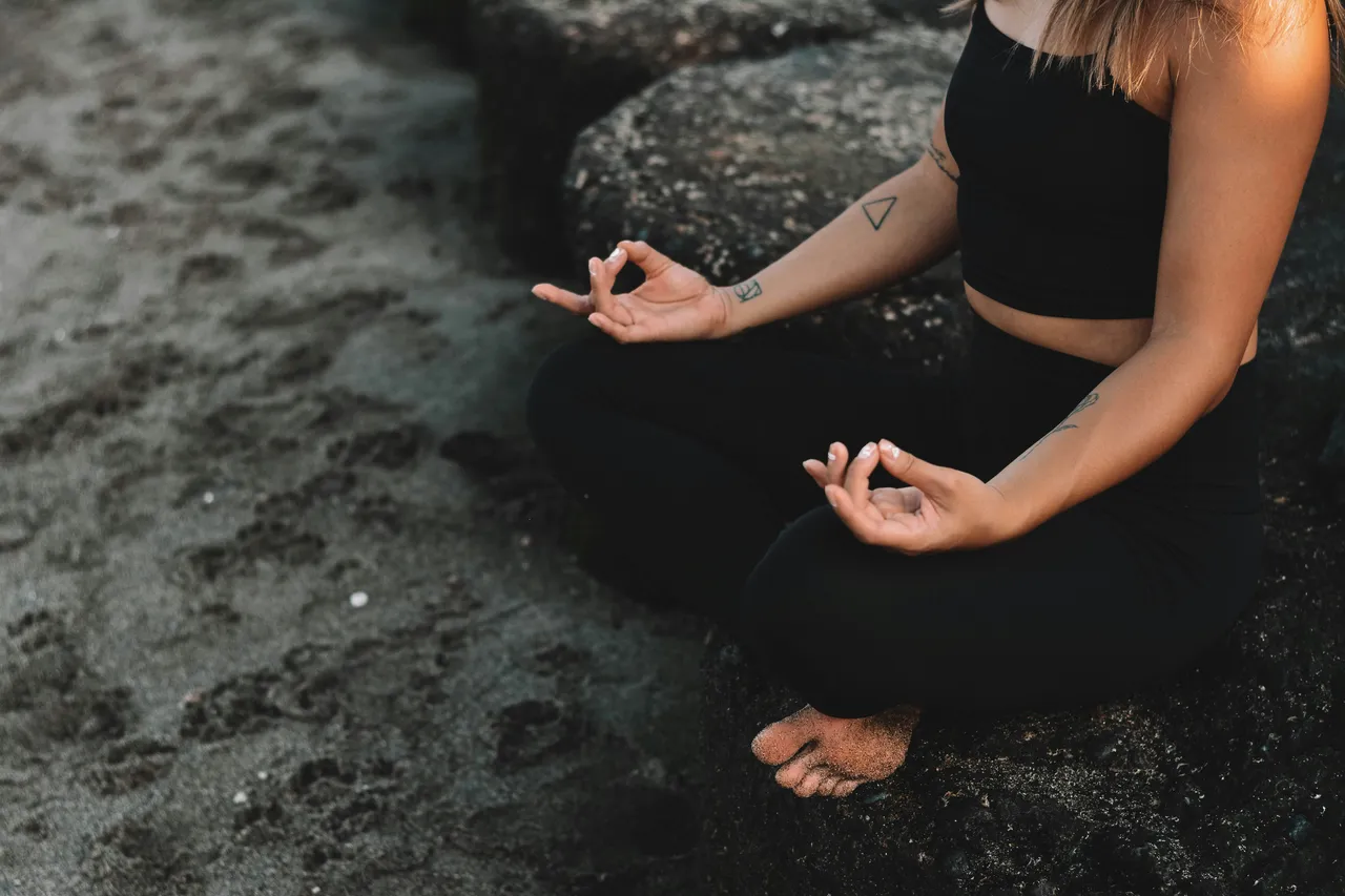 Someone sitting cross-legged on dark sand, hands resting open on their knees