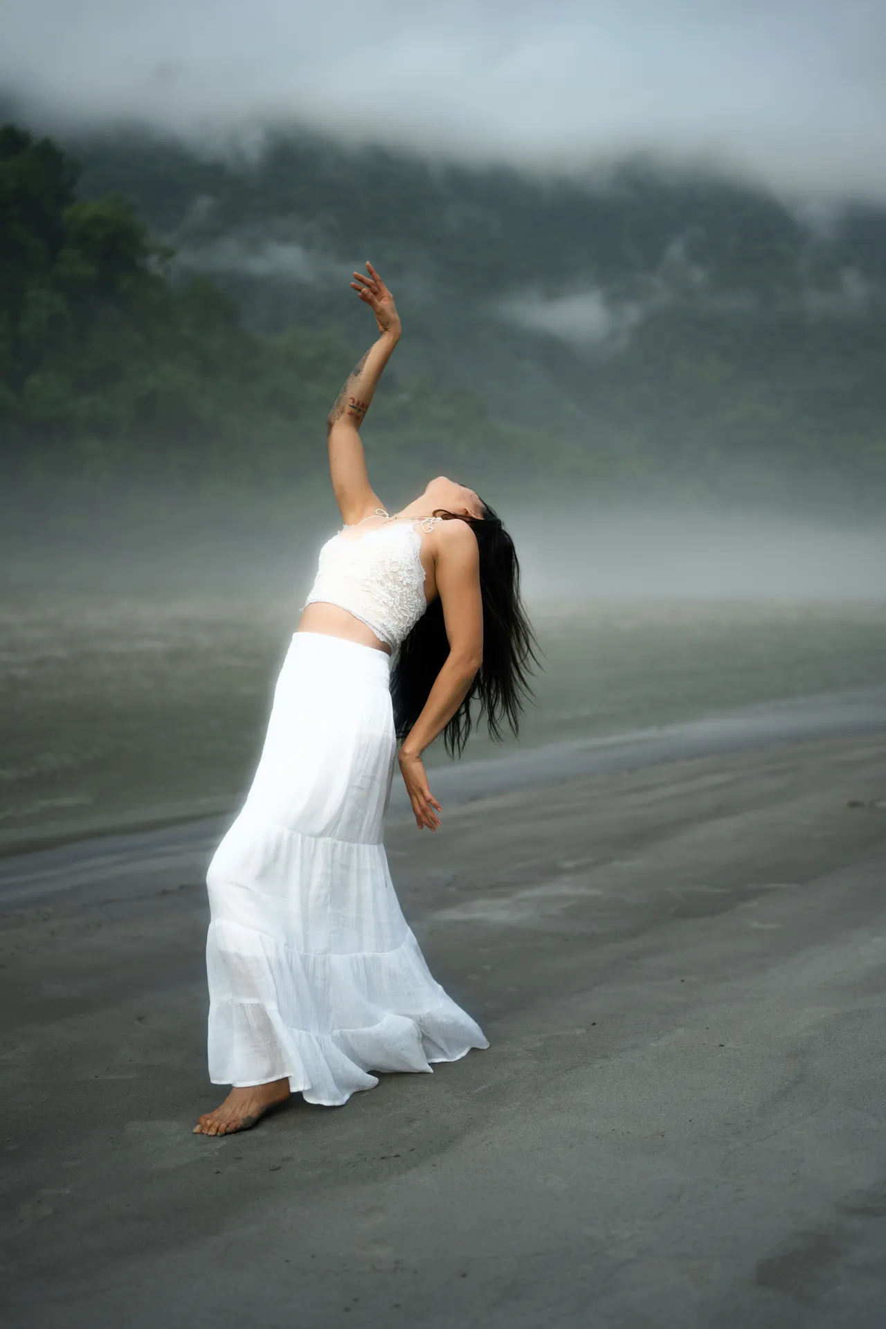 A barefoot dancer arching back on misty grey sand, one arm raised