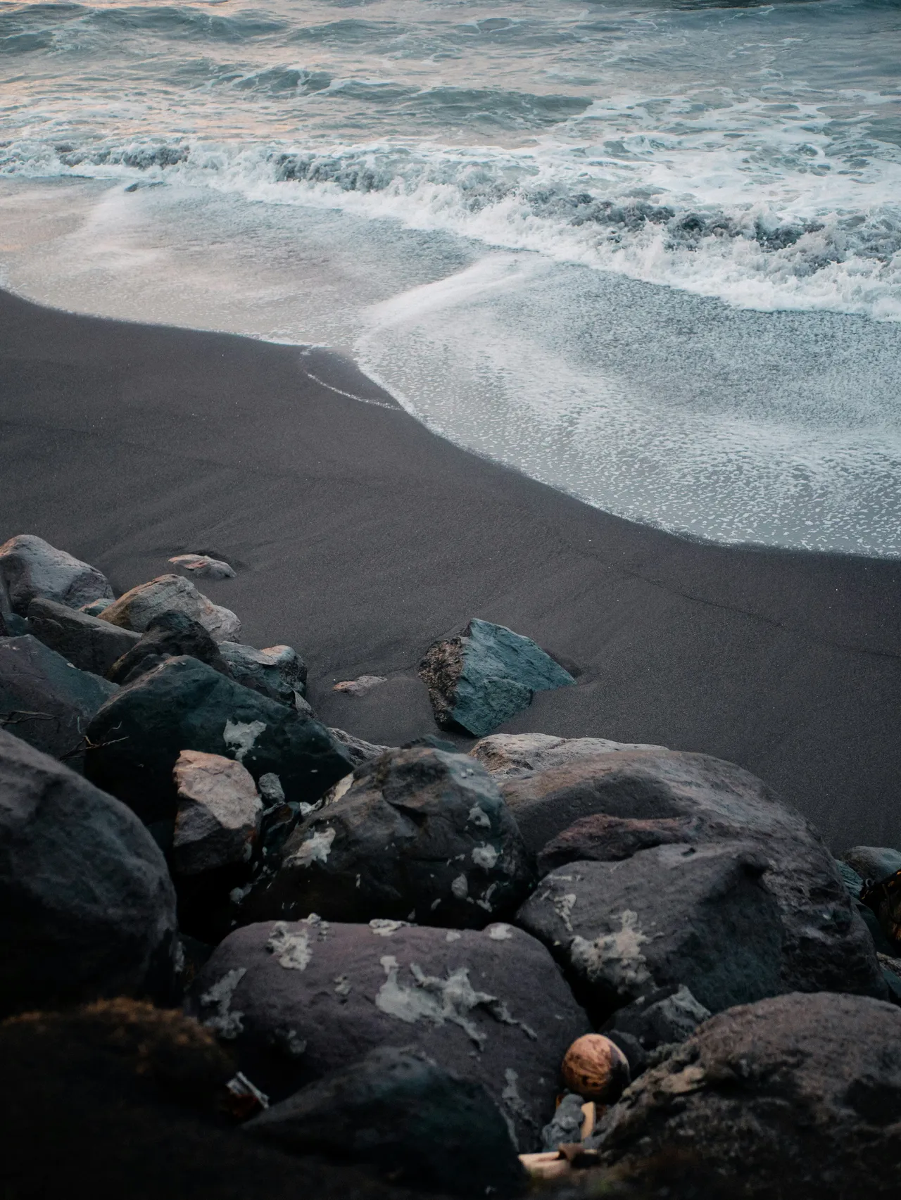 Waves washing over dark sand beside a bank of wet boulders